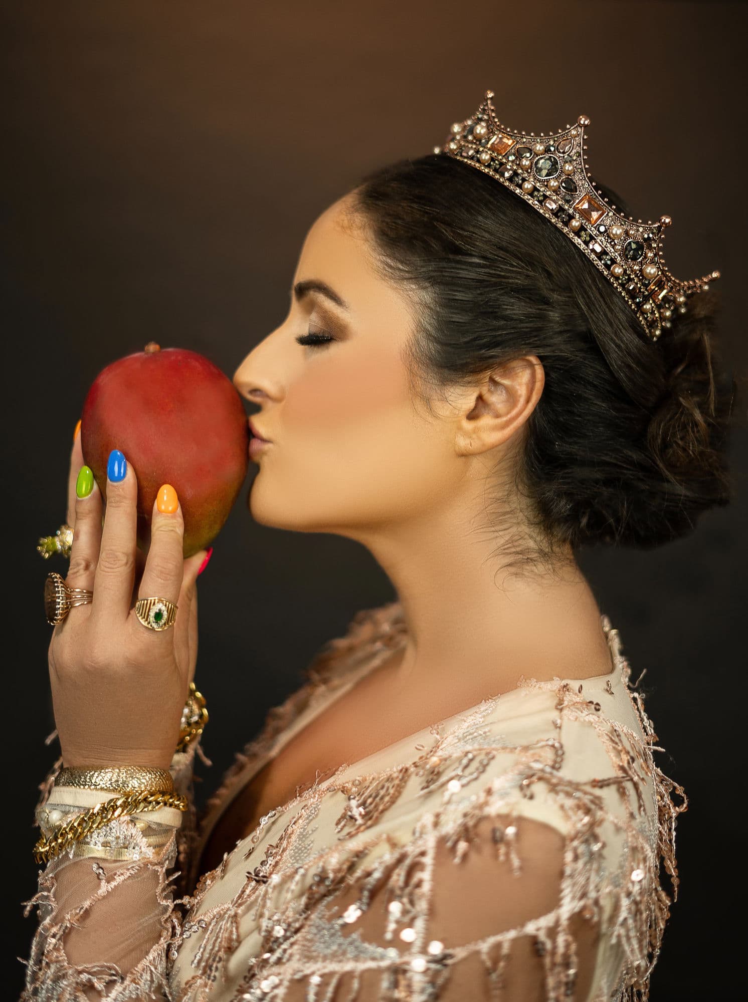 Charlotte in profile wearing a jeweled crown and beaded gown, tenderly kissing a ripe mango